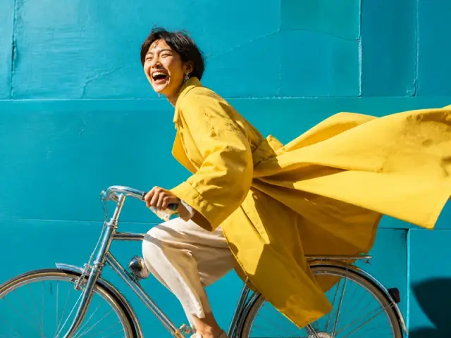Cyclist in a yellow coat riding past a turquoise wall