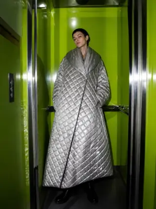 Model in a silver quilted coat inside a fluorescent green elevator